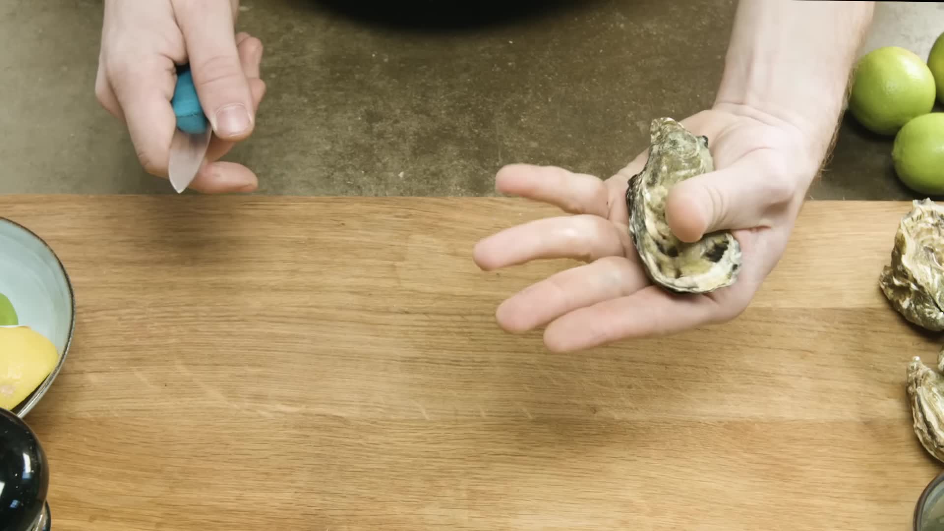 Hand holding oyster, oyster knife nearby.